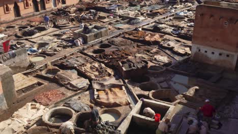 4k uhd scene of traditional moroccans at their work standing in tubs, tanning leather and the dye process in the leather manufacturing area of marrakesh with shops of  merchants in the narrow streets.