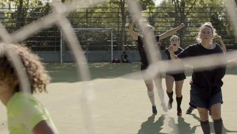 front view of a female football player kicking a penalty and scoring a goal, then celebrating with her team