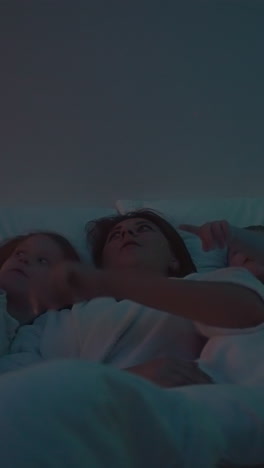 madre y los niños apuntan con los dedos al techo con estrellas de demostración de diferentes colores. luz nocturna y entretenimiento antes de dormir cámara lenta