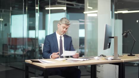 unhappy mature businessman reviewing checking document frustrated by financial report, unhappy sitting in a modern office at a computer desk reading bad news confused by unexpected