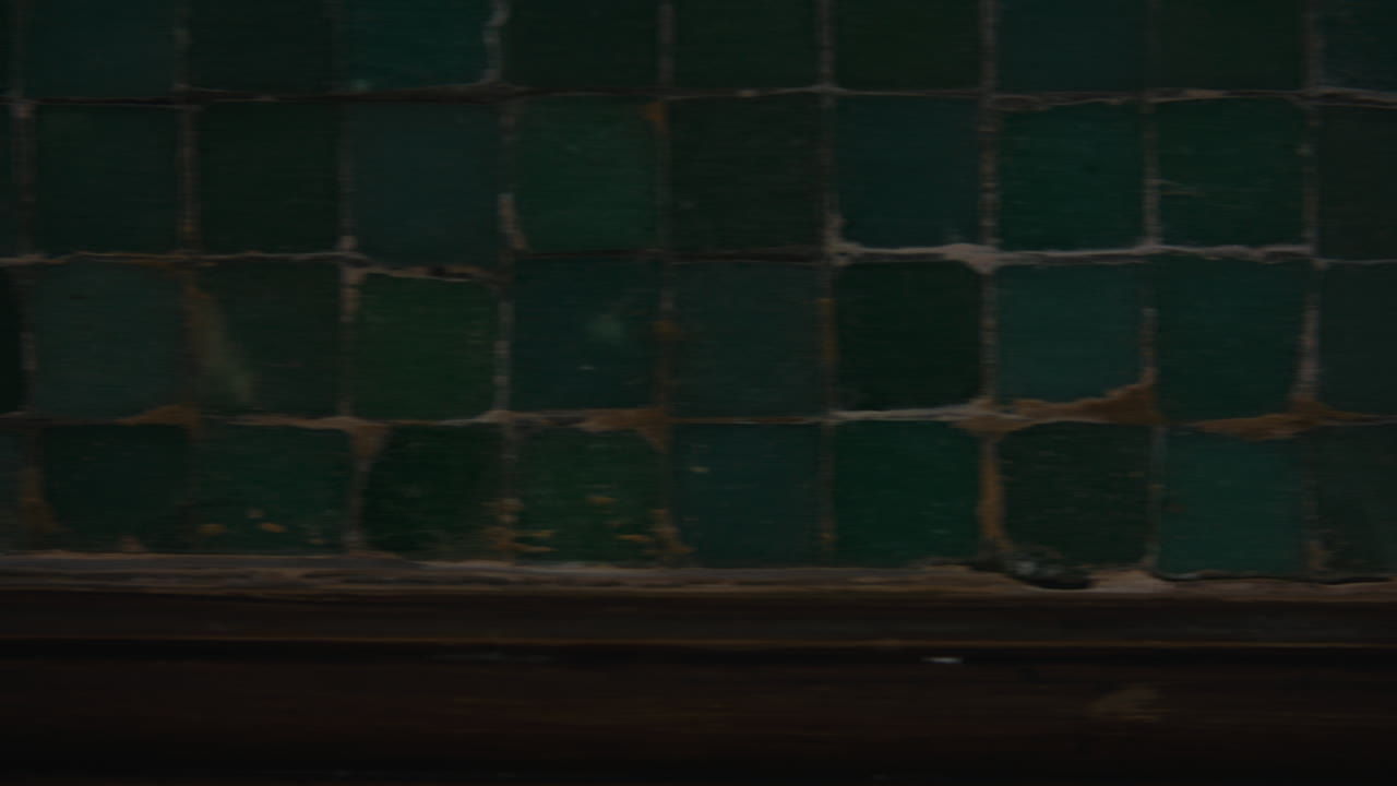 The camera glides left to right, revealing a textured wall of aged green tiles with worn edges and deep patina, suggesting history and craft