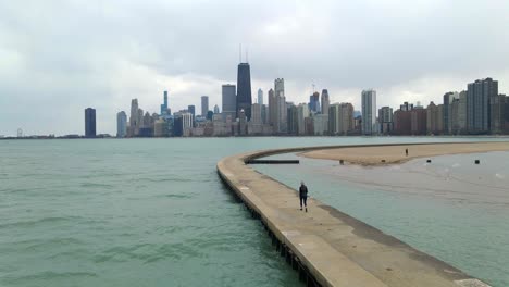 Persona-Caminando-En-El-Lago-Michigan,-El-Centro-De-Chicago-Visto-Al-Fondo,-Viajar-Y-Visitar-Illinois