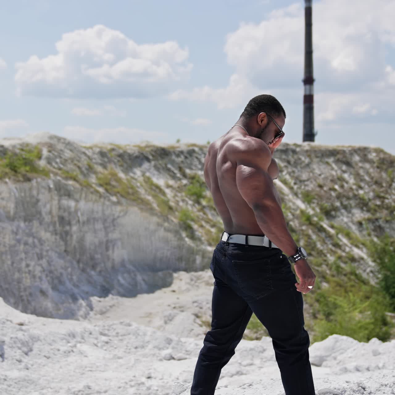 Athletic african man without shirt walks on hill. Muscular dark skinned sportsman among nature in summer. Slow motion