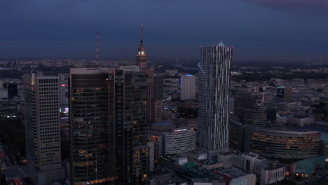 Evening-slide-and-pan-footage-of-downtown-skyscrapers.-Revealing-historic-Russian-style-Palace-of-Culture-and-Science-between-modern-buildings.-Warsaw,-Poland