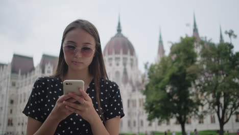 woman using phone in front of the hungarian parliament building