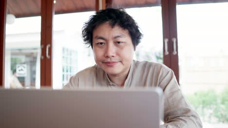 focused asian man looking at silver laptop computer in the cafe during daytime