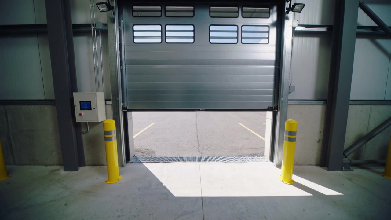 Control panel activating motor, roll-up door opening in loading bay, revealing yellow bollards