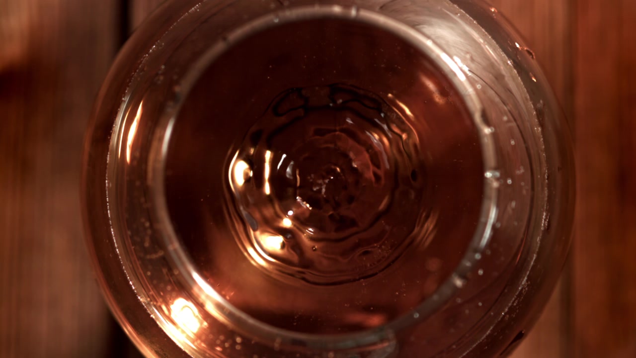 Goccia che schizza al rallentatore in un bicchiere di distillato ambrato