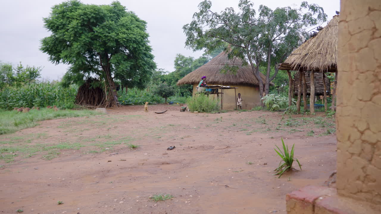 An old African woman washes dishes in rural mud housing homestead