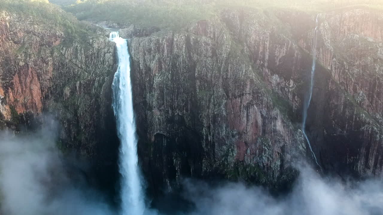 video cinematográfico de un dron desde una cascada alta que deja caer agua en lo profundo de los acantilados de alta montaña de australia