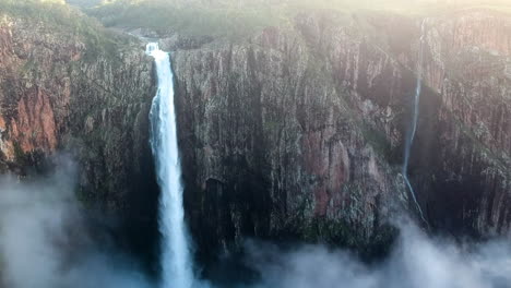 Video-Cinematográfico-De-Un-Dron-Desde-Una-Cascada-Alta-Que-Deja-Caer-Agua-En-Lo-Profundo-De-Los-Acantilados-De-Alta-Montaña-De-Australia