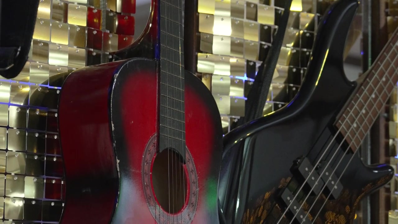 Bir müzik dükkanında yan yana duran bir gitar ve elektro bas. Güneş pencereden içeri parlayarak enstrümanların üzerine ışık düşürüyor. Müşteriler dükkanı geziyor ve çeşitli müzik ekipmanlarını inceliyor.
