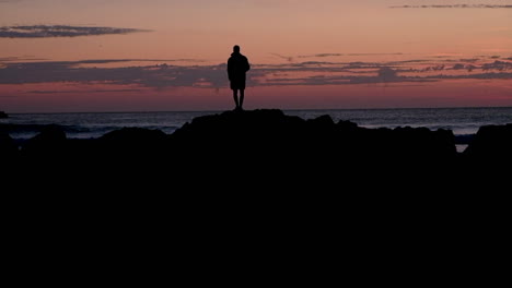 a man standing on the rocks looking out to sea at sunset