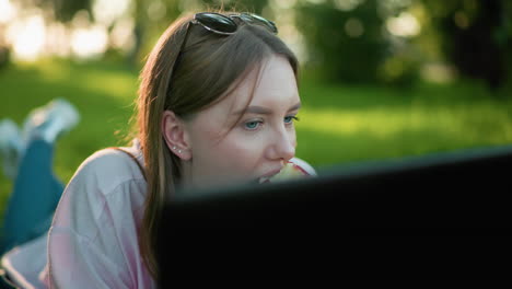 dama blanca con gafas descansando en la cabeza acostada en la hierba sonriendo cálidamente mientras toma un bocado de manzana en su mano, disfrutando de un momento relajado al aire libre, rodeada de vegetación