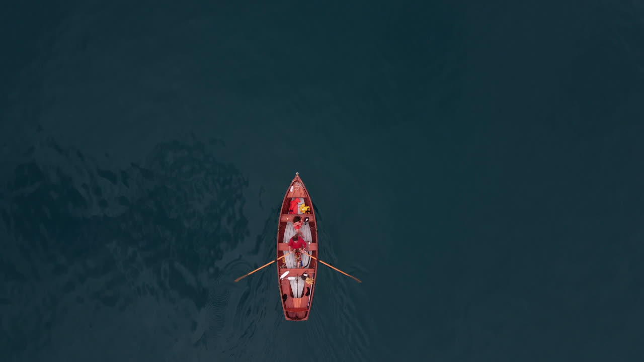 Top down aerial view of a people paddling in a red paddling boat on the deep turquoise alpine lake Thunersee in Switzerland