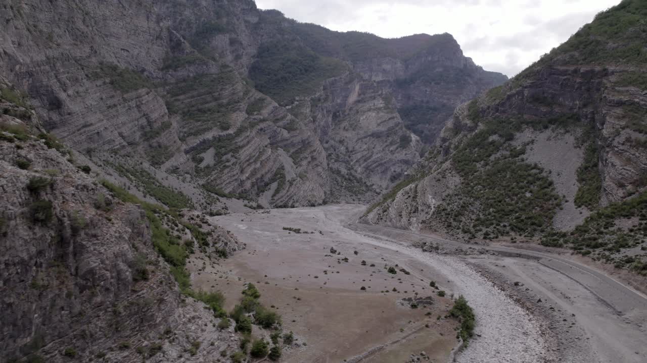video de drones de un plano diagonal que descubre la autopista sh20 entre las montañas y el río cemi en albania a la altura de selce, cielo nublado y camino sinuoso