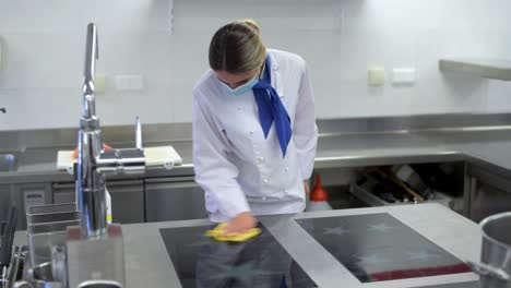 kitchen employee with face mask disinfects and cleans the hotplate