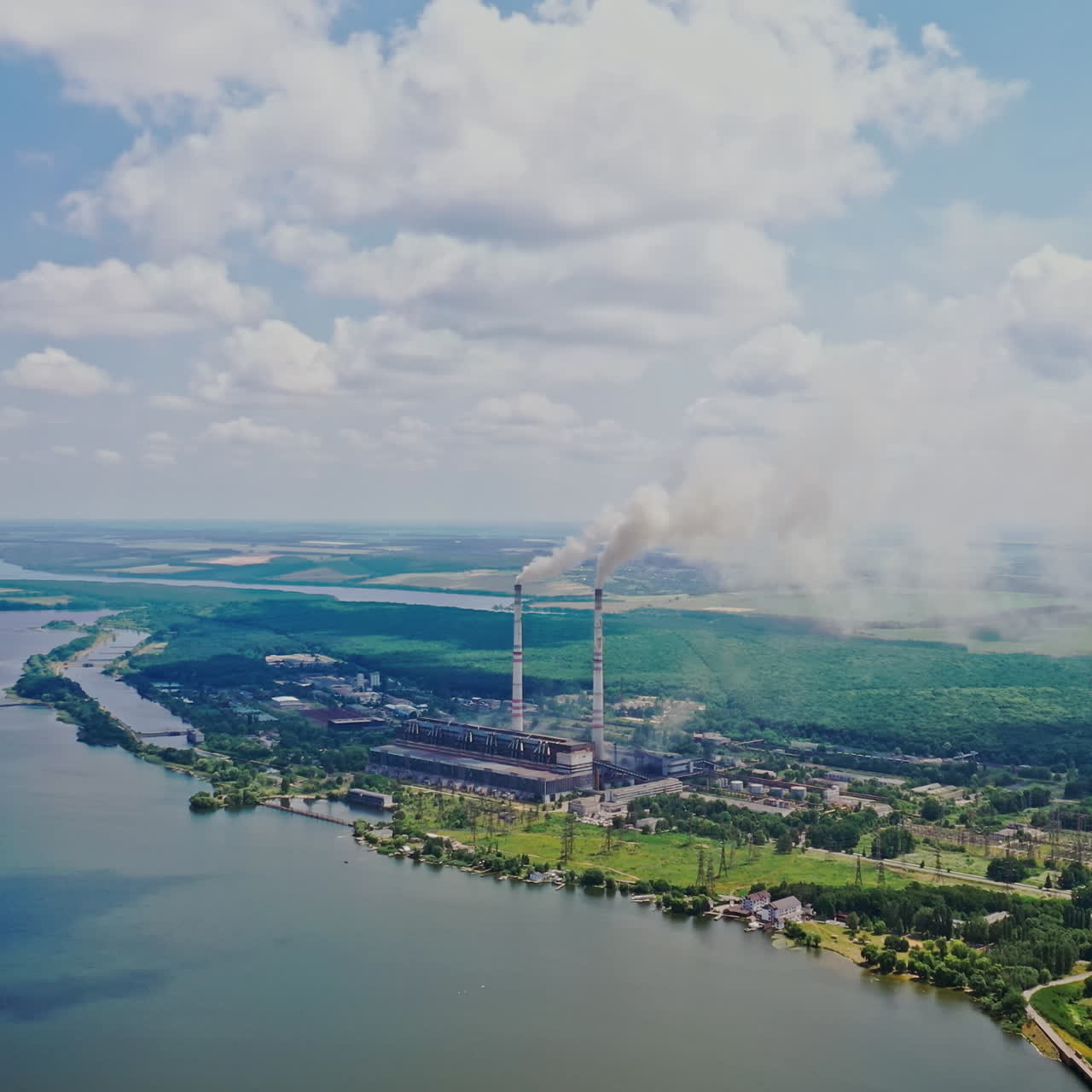 Natural environment of fields, forests, a wide river and factory polluting the air. Pipes with smoke from the big plant near the river. Ecological problem.