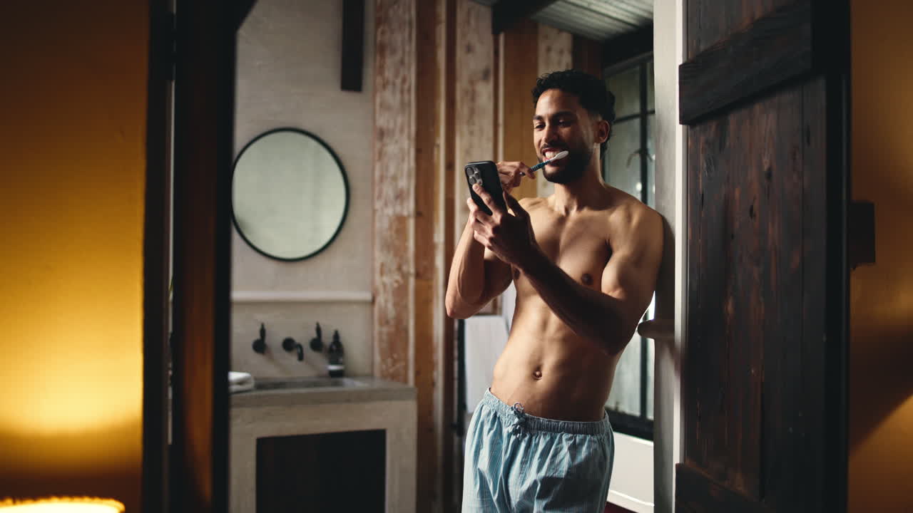 Giovane uomo che si spazzola i denti e usa lo smartphone in bagno