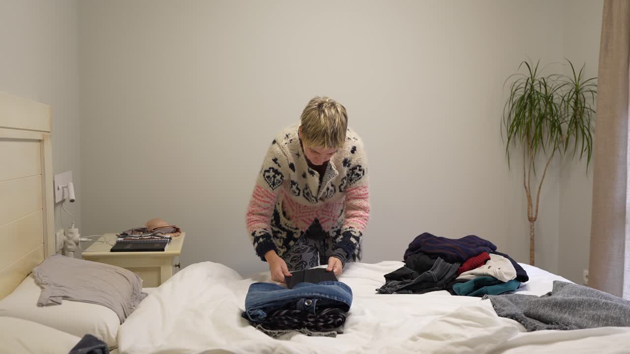 Woman folding clothes on bed in bedroom