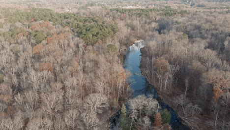 quiet river cutting through leafless forest landscape in fall, aerial