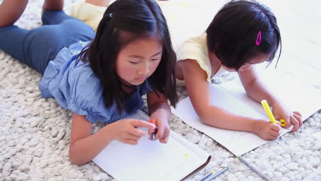 two girls colouring while lying next to each other