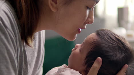 an asian woman kisses her newborn baby girl's forehead a few months old