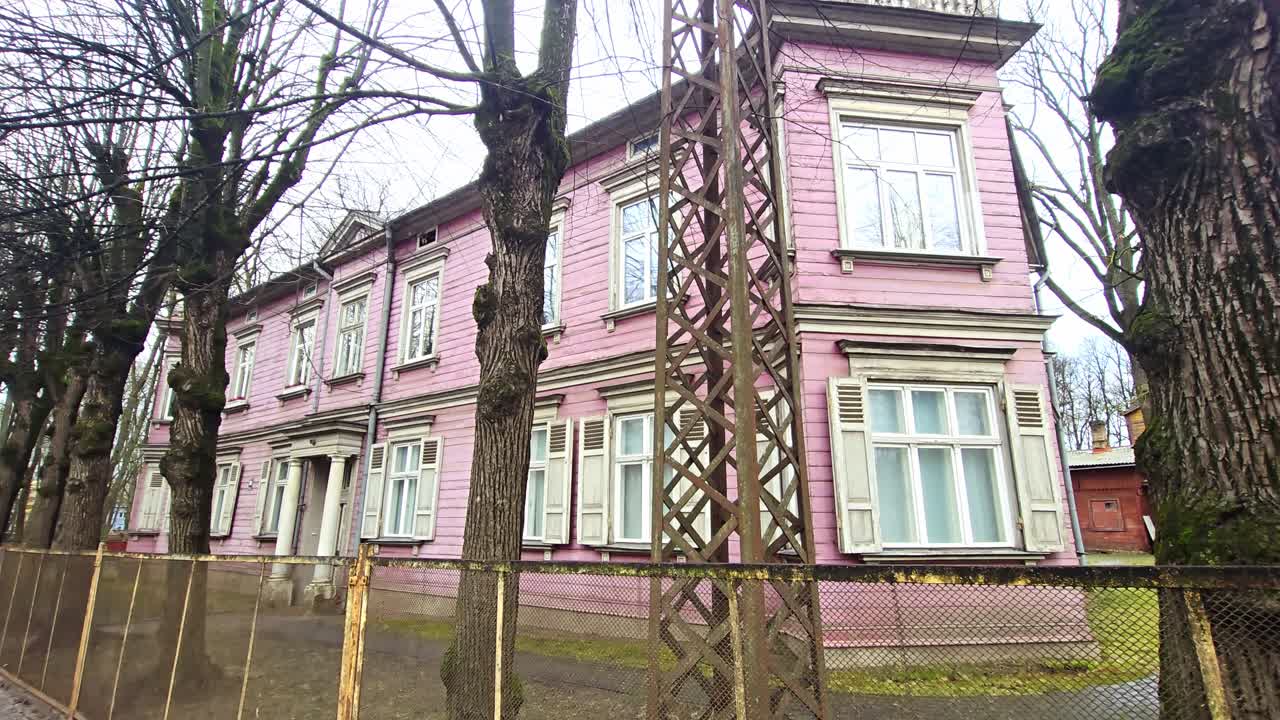 Casa residenziale rosa vintage, Riga, dettagli ornati e tranquilla vista sulla strada.
