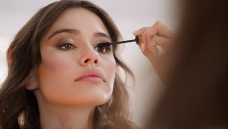 young woman uses wand to apply black mascara on eyelashes