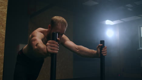 a powerful man pushes a heavy weight trolley in the gym in slow motion. bearded man with vapor on his body trains