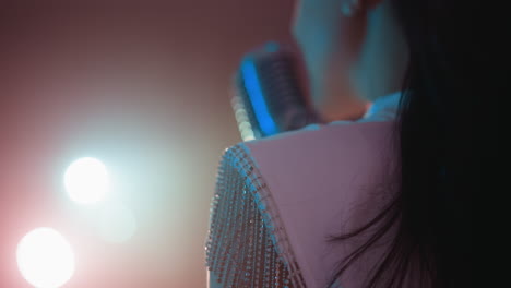 primer plano de una cantante en un vestido blanco adornado con franjas de cuentas, actuando con un micrófono vintage. las luces suaves y brillantes en el fondo mientras se mueve suavemente