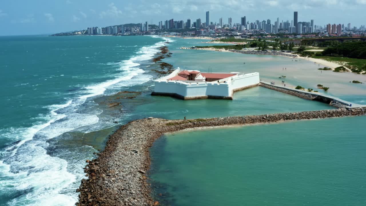 Dolly in aerial drone wide shot of the historic star shaped Reis Magos fort built on a reef with the coastal capital city of Natal in Rio Grande do Norte, Brazil in the background on a warm summer day