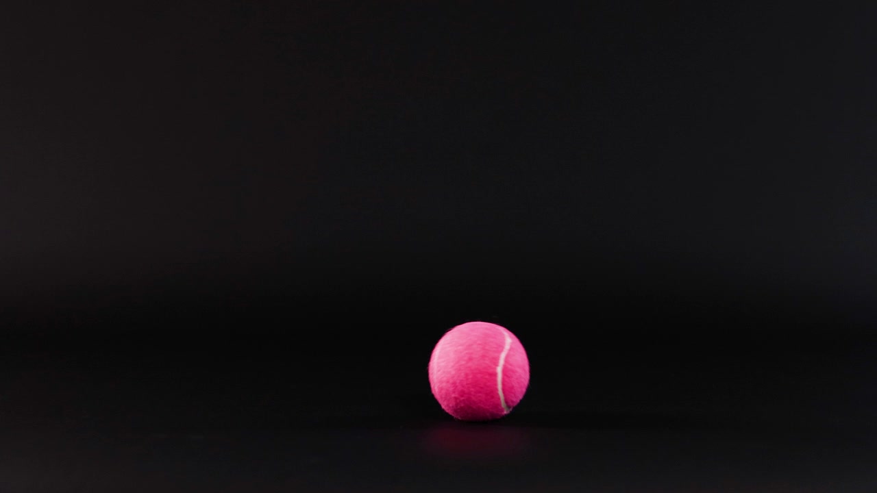 Pink tennis ball rolling across a dark surface