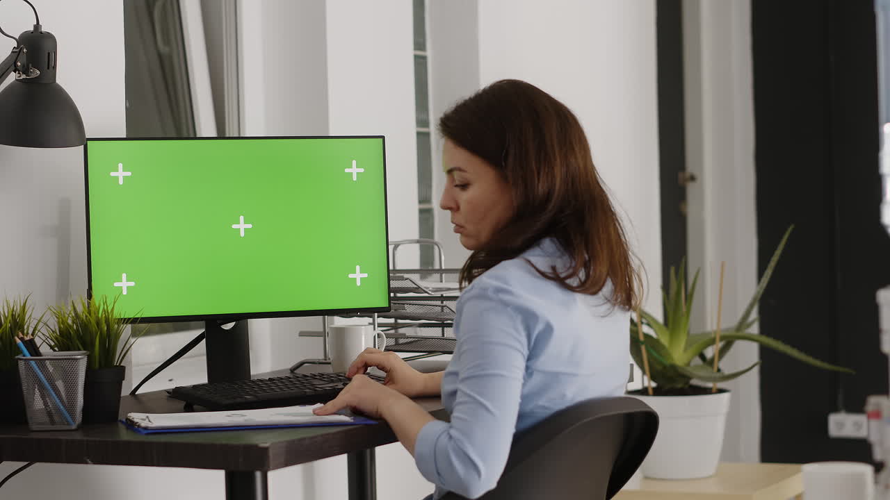Woman working at a desk with a computer with a green screen