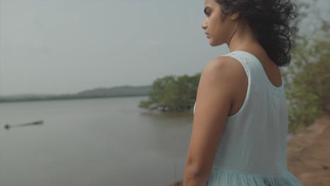 Toma-Panorámica-En-Cámara-Lenta-De-Una-Hermosa-Mujer-De-Moda-Vestida-Con-Un-Top-Azul-Bebé-Mirando-Pensativamente-Al-Otro-Lado-Del-Lago