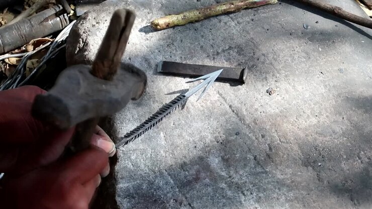 Datoga tribe man hammering a handmade arrow on a rock outside