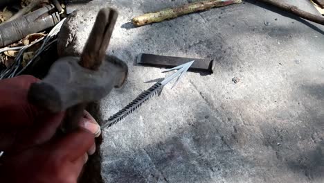 Datoga tribe man hammering a handmade arrow on a rock outside