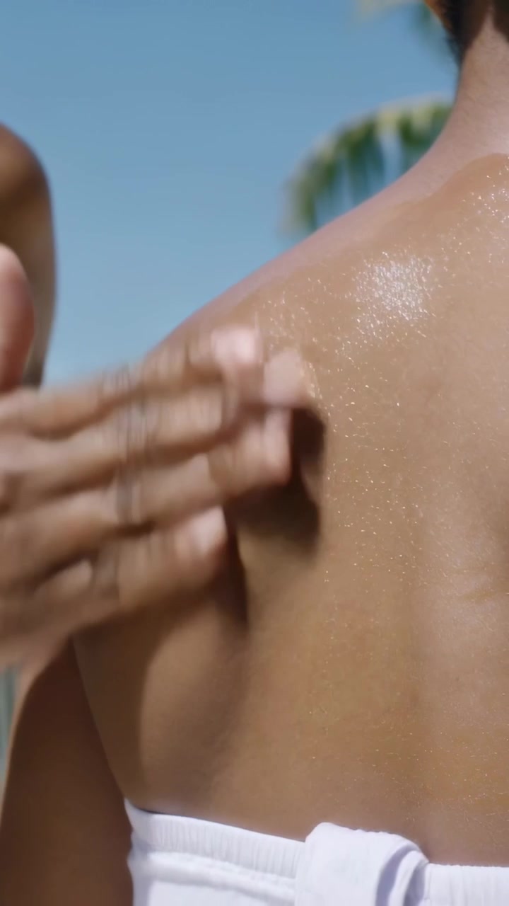 Vertical video: Spraying white bottle, woman rubbing SPF on friend in bikini at beach for sun care