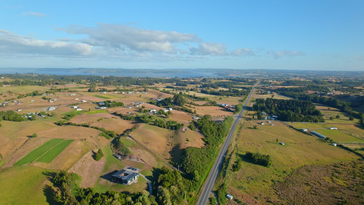 fotografía aérea ascendente de una carretera en medio de las tierras de cultivo de chiloe soleada, chile