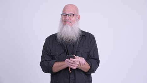 happy mature bald bearded man thinking while using phone