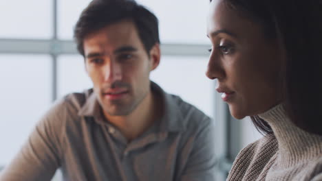 Pull-Focus-Close-Up-Of-Businesswoman-Working-On-Laptop-At-Desk-With-Male-Colleague