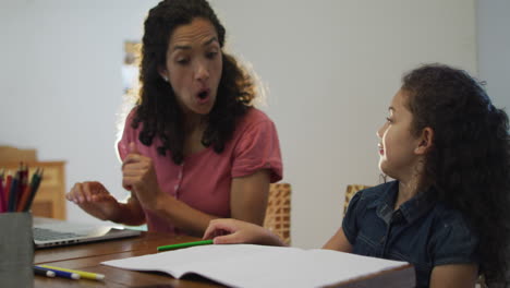 happy biracial mother and daughter doing homework together at home