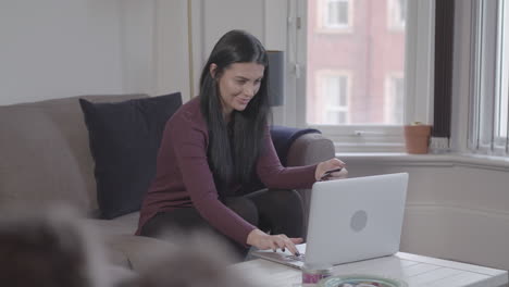 Weite-Aufnahme-Einer-Jungen-Attraktiven-Dame,-Die-Einen-Laptop-Benutzt,-Um-Etwas-Online-Zu-Kaufen,-Lächelt,-Sobald-Sie-Einen-Kauf-Getätigt-Hat---Unbenotet