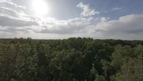 Epic low-altitude drone flight just above treetops, under radiant sunlight with blue sky and clouds — a majestic, peaceful aerial scene with a near-biblical sense of elevation
