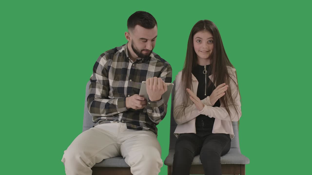웃긴 십대 소녀는 손을 지 않는 몸짓을 하며, 남자는 태블릿 화면을 보여주고 이야기합니다. 아버지와 딸은 인터넷을 서핑하거나 소셜 미디어를 사용합니다. chromakey, 녹색 화면, 시네마 4k prores hq.