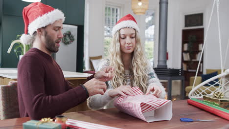 happy diverse couple sitting at table packing christmas presents at home, in slow motion