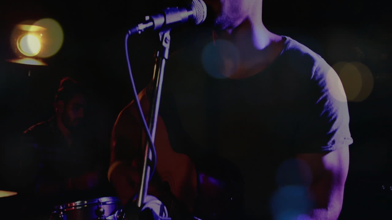 Membri della band che si esibiscono su un palco in penombra nell'industria musicale, con barre di onde sonore fluttuanti e icone di batteria.