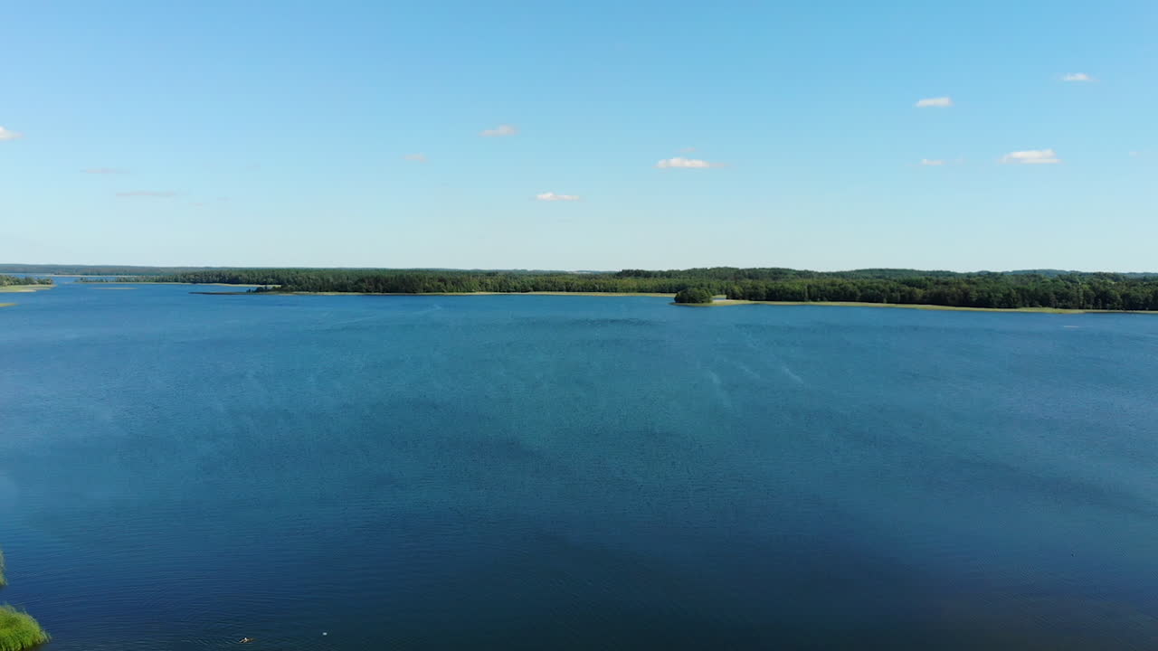 аэрофотосъемка: беспилотник поднимается над красивым голубым озером, на горизонте видна линия леса