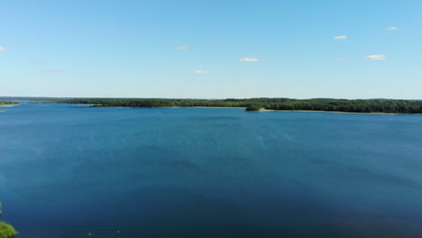 aerial: drone lift up above beautiful blue lake with forest line visible in the horizon