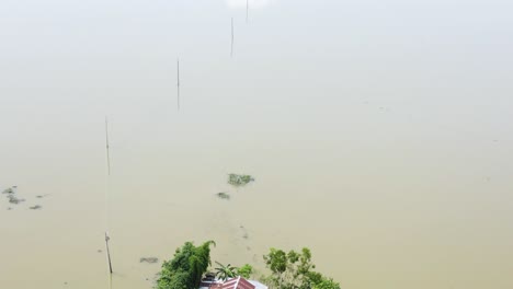 a rural house is surrounded by floodwaters in the haor area, reflecting the recurring flood challenges in sylhet, bangladesh, south asia - aerial ascend shot